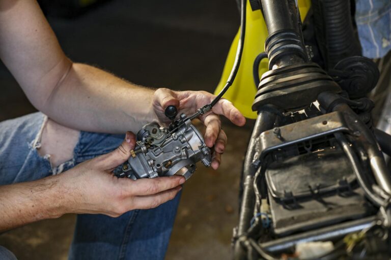 Close-up shot of a mechanic's hands repairing a motorcycle carburetor indoors.