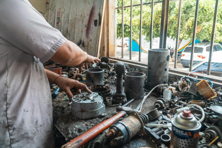 Mechanic arranging car parts on a cluttered work table in an automotive workshop.